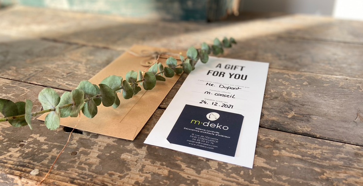 Carte cadeau M·DEKO « A GIFT FOR YOU » posée sur une table en bois, avec enveloppe kraft
